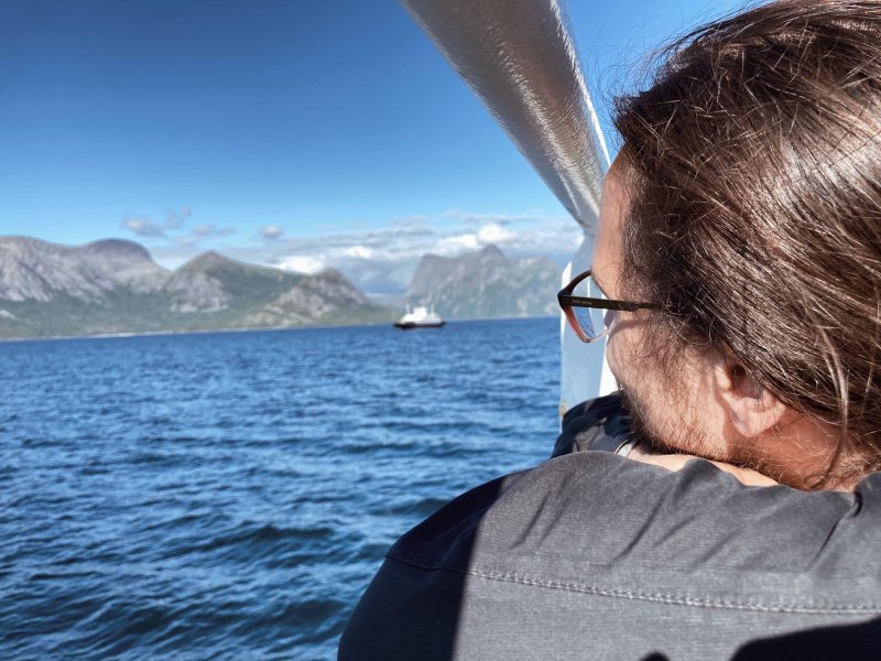 person som ser ut uttover blått hav med ein ferje og fjell i bakgrunnen