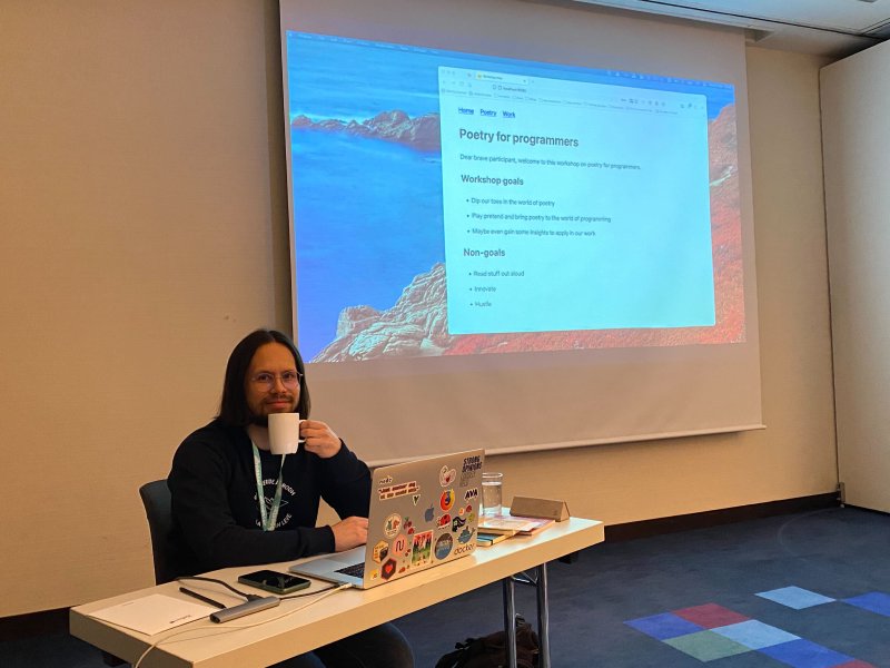 a person holding a cup of coffee looking into the camera with a powerpoint presentation behind