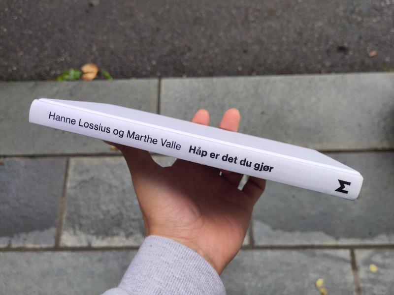 Hånd som holder en bok med teksten Hanne Lossious og Marthe Valle, Håp er det du gjør.