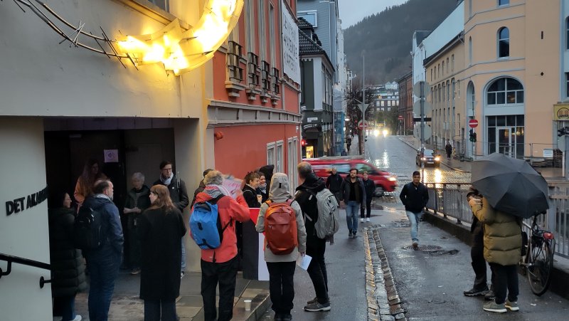 mennesker med palestinaskjerf, som prater sammen ved inngang til konferanse. Person kommer gående opp bakken og ser på dei.