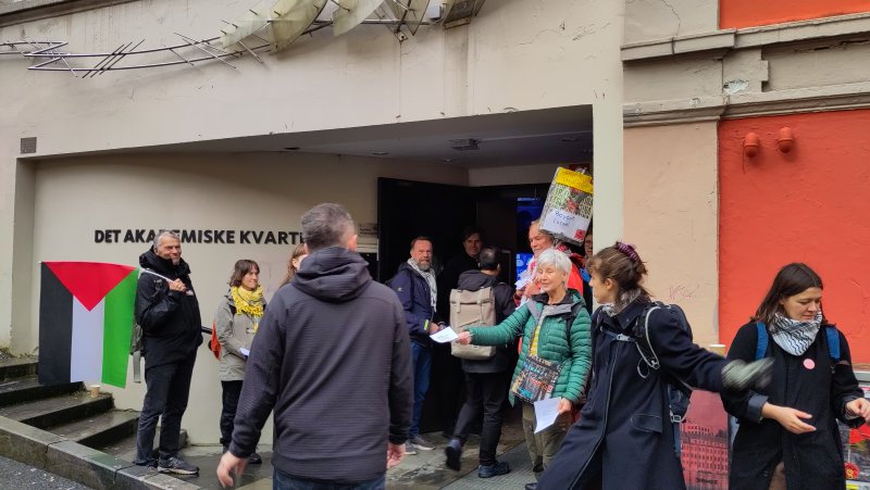 mennesker i palestinaskjerf som deler ut flygeblader til person som er på vei inn i konferansen.