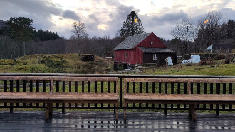 utsikt mot eit jorde med eit raudt gardshus i bakgrunnen